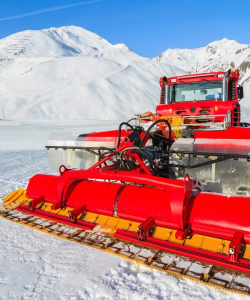 Red snow groomer on ski slope